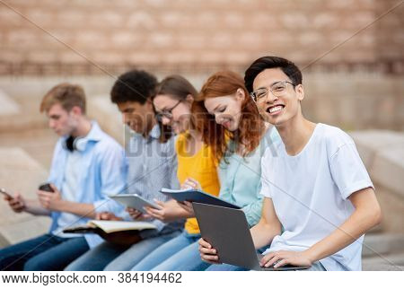 Asian Student Learning With Coursemates Sitting Outside University Building. Students Life Concept. 
