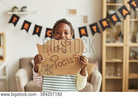 Modern Joyful African American Boy Standing In Living Room Decorated For Halloween Holding Cardboard
