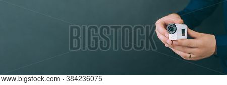Banner. White Action Video Camera, In The Hands Of A Guy On A Black Background In The Studio.