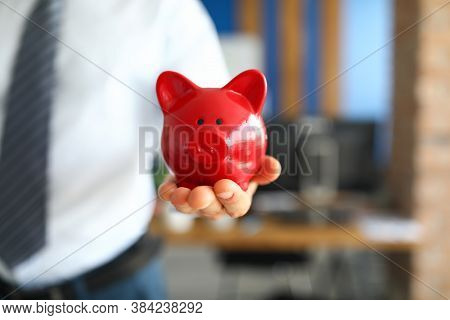 Close-up Of Businessman Holding Red Piggy Bank. Stylish Interior Design In Office. Save Money For Fu