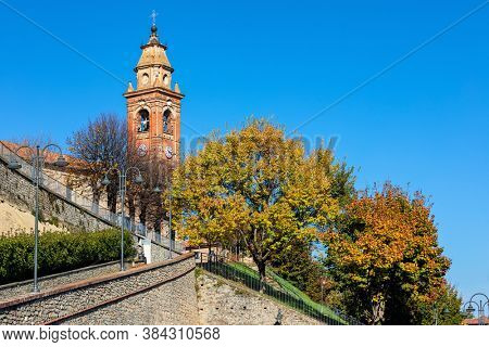 Old church belfry and colorful autumnal trees under blue sky in small town of Diano d'Alba in Piedmont, Northern Italy.