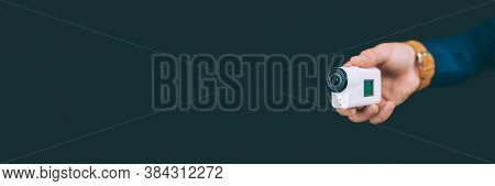 Banner. White Action Video Camera, In The Hand Of A Guy On A Black Background In The Studio.