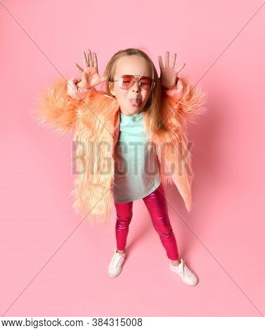 Trendy Little Girl In Pink Glasses, Blue Shirt, Glossy Leggings And Fluffy Coat Teasing Someone Loll