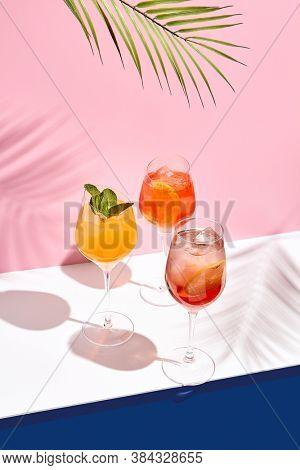 Spritz cocktail set on white table. Tropical palm leaf shadow. Summer cocktail group. Pink and classic blue background