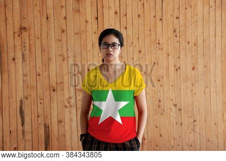 Woman Wearing Myanmar Flag Color Shirt And Standing With Two Hands In Pant Pockets On The Wooden Wal