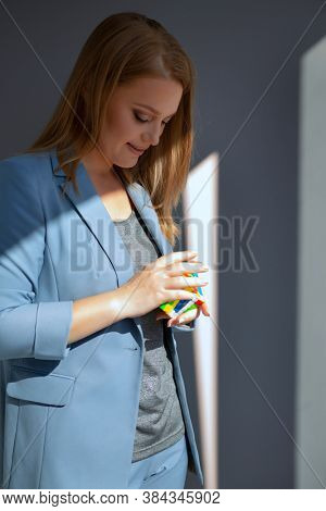 Beautiful and clever business woman wearing light blue summer suit posing indoor holding in her hand toy mind-breaker over gray wall, natural light