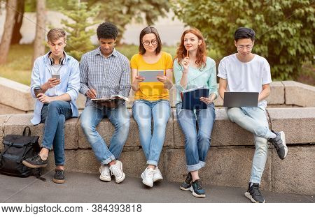 Diverse Students Learning Using Laptop And Tablet Computers Sitting Together In University Campus Ou