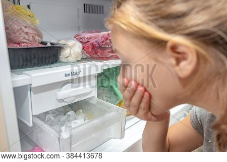 A Surprised Girl Looks At The Full Ice Cube Tray Of The Freezer Ice Maker.