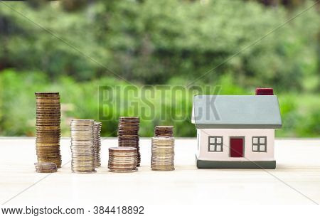 Small House And Columns Of Coins On A Green Background. The Concept Of Buying, Selling, Renting Real