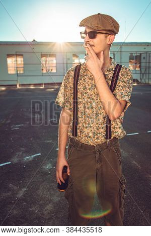 Young Hipster Man In Retro Clothing Smokes While Holding Beer In Hand