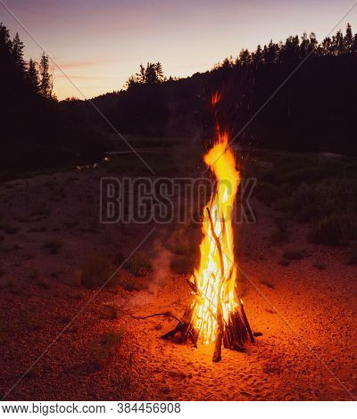 Traditional Midsummer Ligo Celebration In Latvia. Huge Bonfire On The River Shore In The Forest. Pur