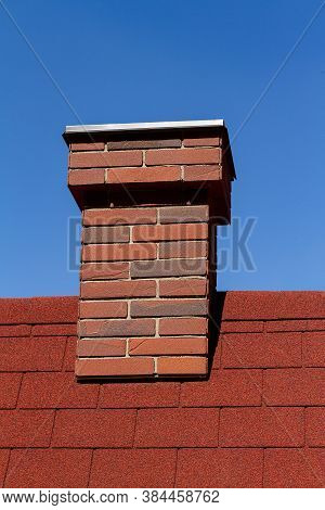Red Brick Chimney On Red Roof With Blue Sky Behind