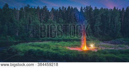 Traditional Midsummer Ligo Celebration In Latvia. Huge Bonfire On The River Shore. Scenic Landscape 