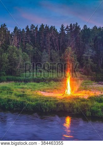 Landscape Of Forest And River At White Night. Huge Bonfirefire. Traditional Midsummer Ligo Celebrati