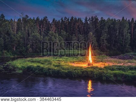 Midsummer Ligo Celebration. Huge Bonfire On The River Shore. Scenic Landscape Of Forest At White Nig