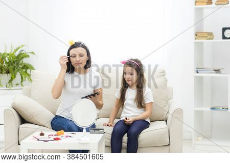 Mother And Daughter Are Doing Make Up And Having Fun Sitting At Dressing Table At Home.