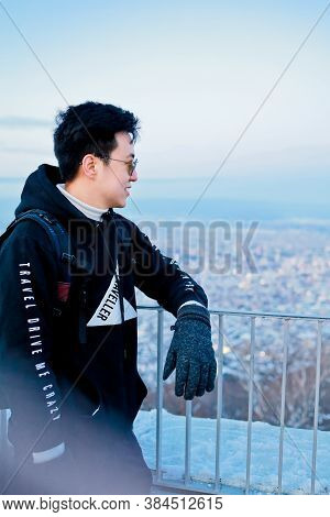 A Man With View From Top Of Mt. Moiwa In Sapporo City, Hokkaido, Japan During Winter With Night City