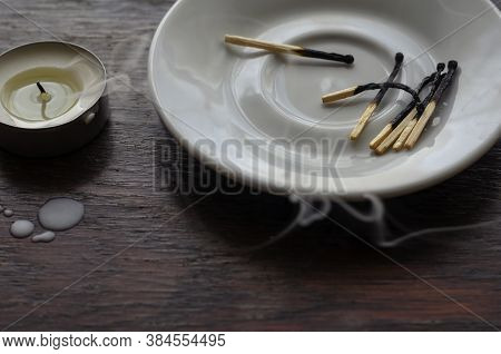 A Darkened Small Candle On A Wooden Table. Next To The Wax Camles On The Table And Burnt Matches In 