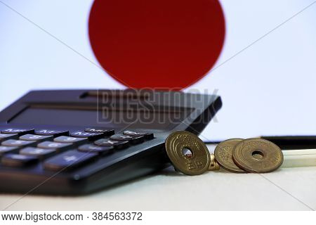 Japanese Five Yen Three Coins (jpy) On White Floor With Black Calculator And Pencil On Japan Flag Ba