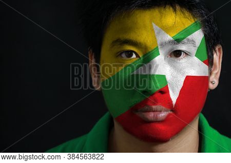 Portrait Of A Man With The Flag Of The Myanmar Painted On His Face On Black Background. Red Green An