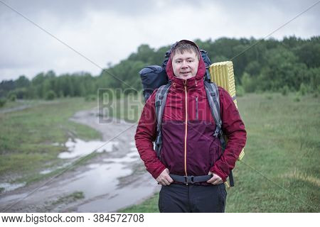 Guy Tourist Hiker Walks Along The Road With A Backpack In A Red Jacket In The Rain