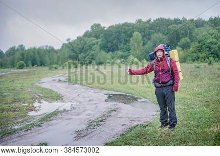 Guy Tourist Hiker Walks Along The Road With A Backpack In A Red