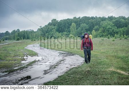 Guy Tourist Hiker Walks Along The Road With A Backpack In A Red Jacket In The Rain