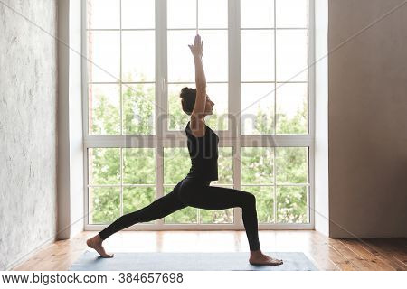 Middle Aged Woman Practicing Yoga, Standing In Warrior One Exercise, Virabhadrasana I Pose, Wearing 