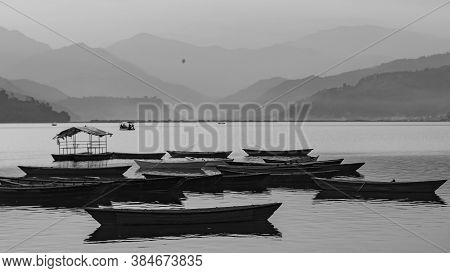 View Over A Few Wooden Boats On Phewa Lake In Pokhara, Nepal With The Surrounding Mountains In The B