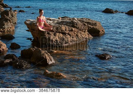 Calm Lady In Pink Bikini Meditating On Rock. Calm Sea. Alone Time. Meditation And Self-absorbed. Spa