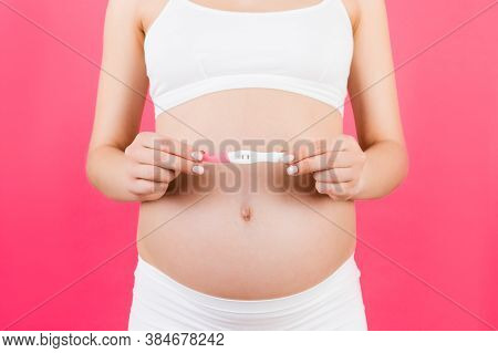 Close Up Of Positive Pregnancy Test Against Pregnant Womans Belly At Pink Background. Future Mother 