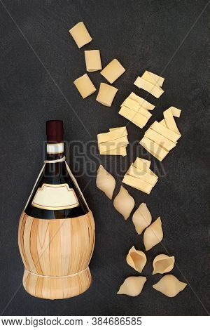 Traditional Italian red wine & pasta with pappardelle, conchigle & pacheri on mottled dark grey background. 