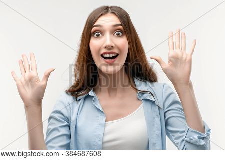Studio Shot Of Surprised Young Female With Long Chestnut Hair, Dressed In Casual Clothes, Smiling Ha