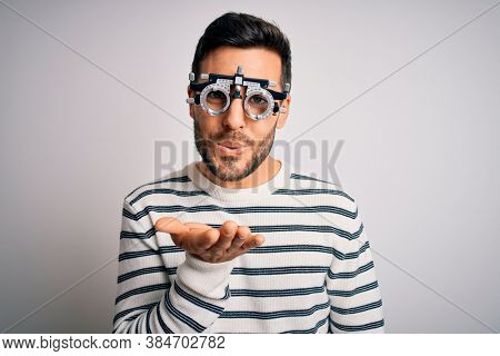Young handsome man with beard wearing optometry glasses over isolated white background looking at the camera blowing a kiss with hand on air being lovely and sexy. Love expression.