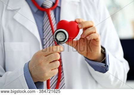 Male Medicine Doctor Holding Red Heart And Putting Stethoscope Head Close To It Closeup. Medical Hel