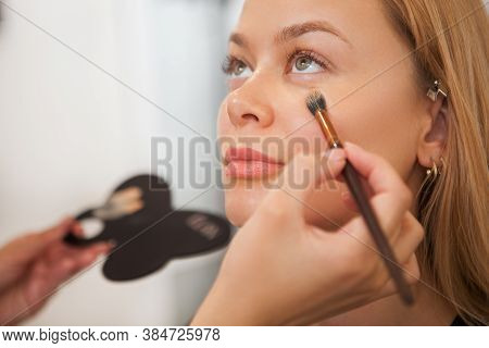 Close Up Of A Beautiful Woman Smiling While Professional Makeup Artist Applying Concealer Under Her 