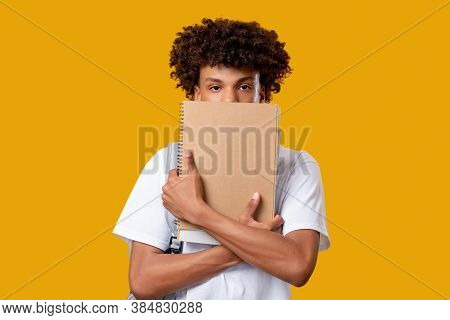 Black Teenager. Exam Worry. Confused Young Male Student Hiding Under Notebook Isolated On Orange Cop