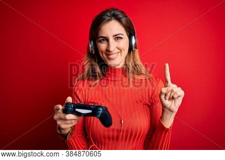 Young beautiful brunette gamer woman playing video game using joystic and headphones surprised with an idea or question pointing finger with happy face, number one