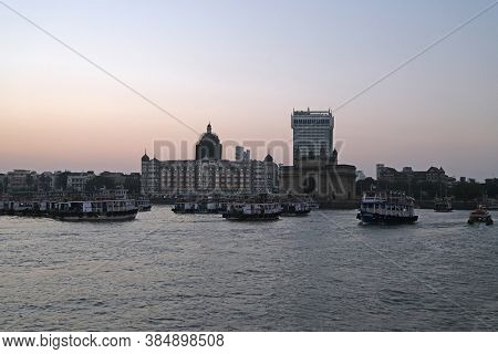 MUMBAI, INDIA - FEBRUARY 15, 2020: Taj Mahal hotel, Gateway of India and tourist boats in water of Arabian Sea on sunset in Mumbai, India