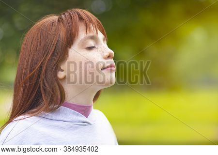 Young Red-haired Girl Inhales Air In The Park. Cute Little Girl Is Resting In Nature In The Fresh Ai