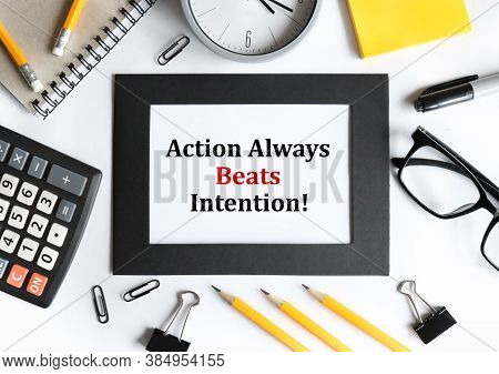 Action Always Beats Intention. Text On White Paper In A Black Frame, Near A Calculator, Pen, Pencil,