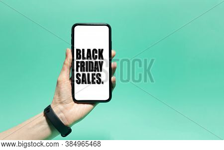 Close-up Of Black Friday Sales Text On White Screen On Smartphone In Male Hand. Background Of Cyan, 
