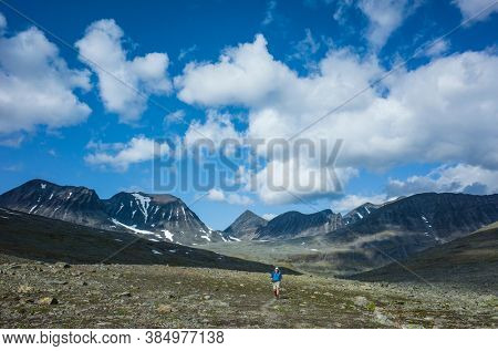 Hiking in Swedish Lapland. Man trekking alone in northern Sweden in Stuor Reaiddavaggi valley. Arctic mountain nature of Scandinavia in summer day blue sky with clouds