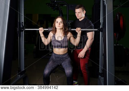 Lesson with a trainer in the gym. The trainer helps the woman to perform the exercise on the Schmitt simulator.