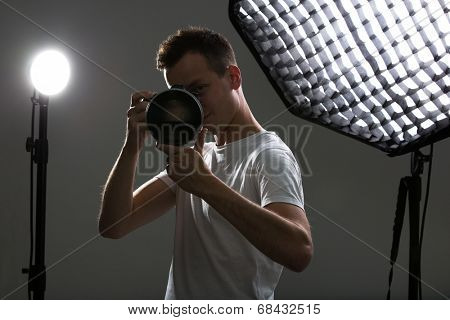 Young pro photographer with digital camera - DSLR and a huge telephoto lens in her well equiped studio, taking photos (color toned image; shallow DOF)