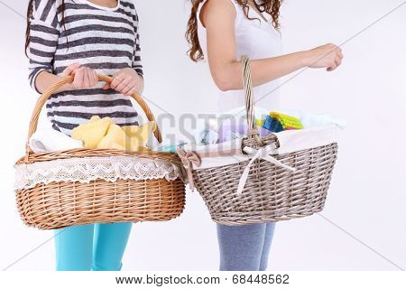 Women holding laundry baskets with clean clothes, towels and pins, isolated on white