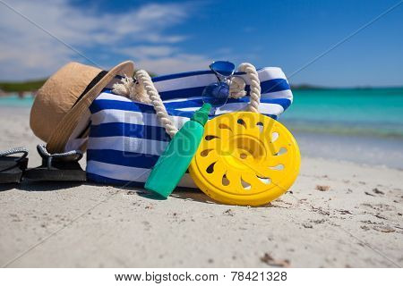 Bag, straw hat, sunblock and frisbee on white sandy tropical beach