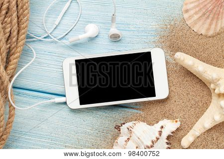 Smartphone on wood and sea sand with starfish and shells. Top view with copy space