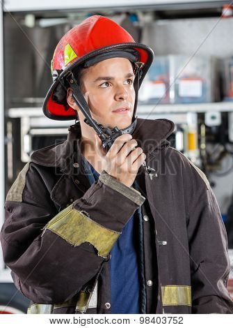 Confident male firefighter looking away while using walkie talkie at fire station