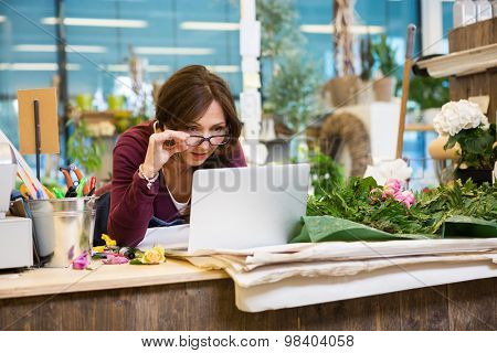 Shocked mid adult female florist holding glasses while using laptop at counter in flower shop